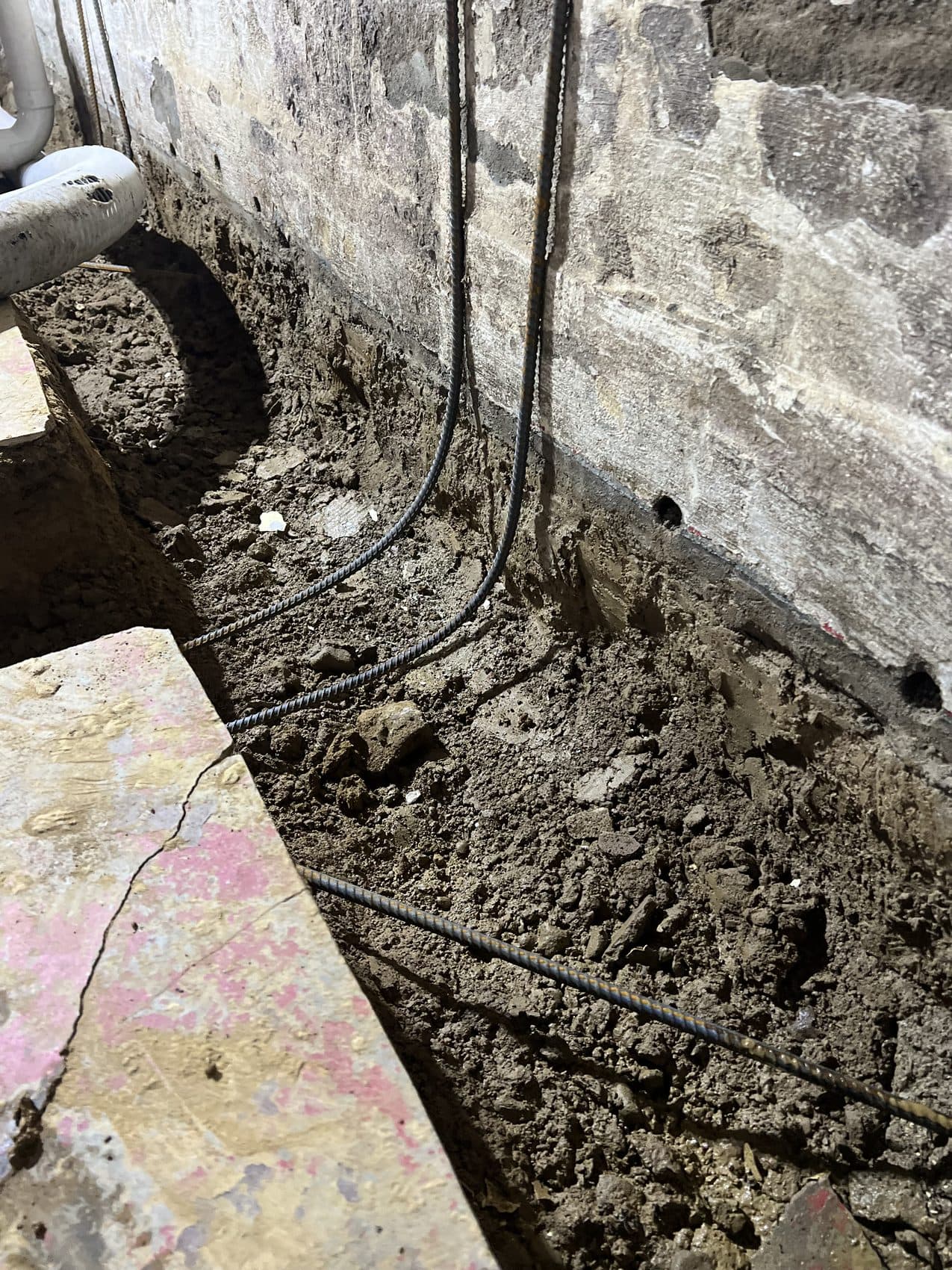 Interior footer trench dug along an old foundation wall with new drain pipe and rebar laid in