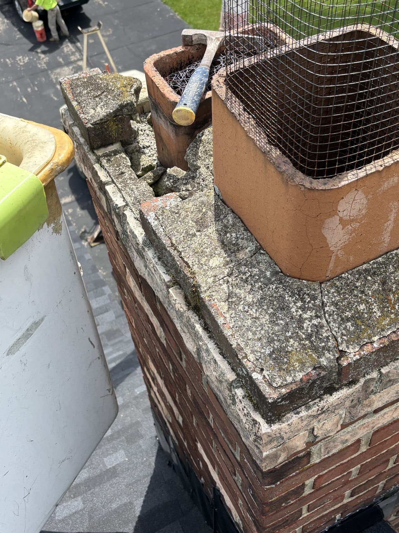 Chimney crown being re-parged around a clay flue with new mesh, roof shingles below