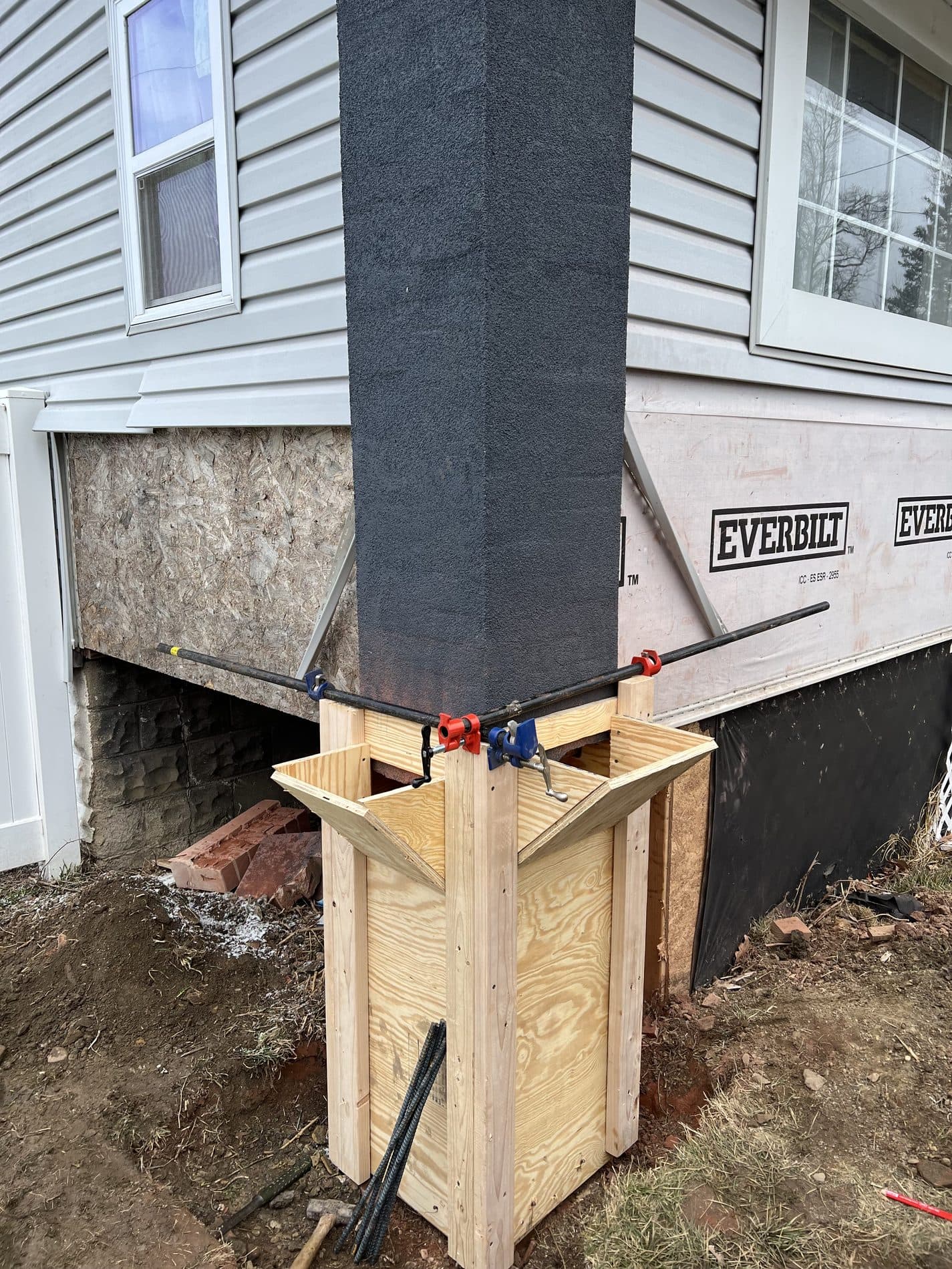 A house corner shored on a clamped plywood cribbing box with rebar outriggers while its foundation pier is rebuilt