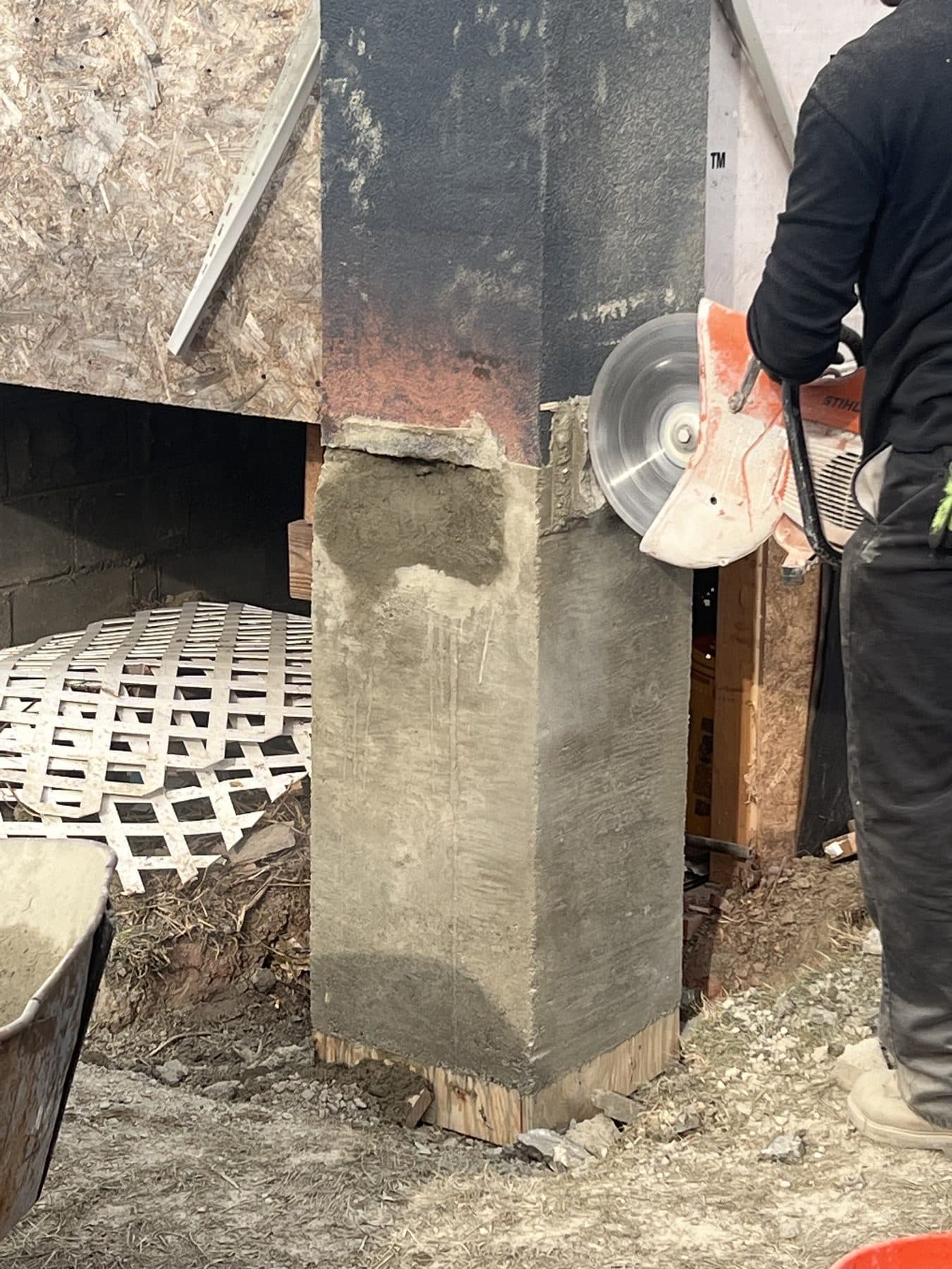 A HydroGuard mason trimming a freshly parged concrete pier with a cut-off saw