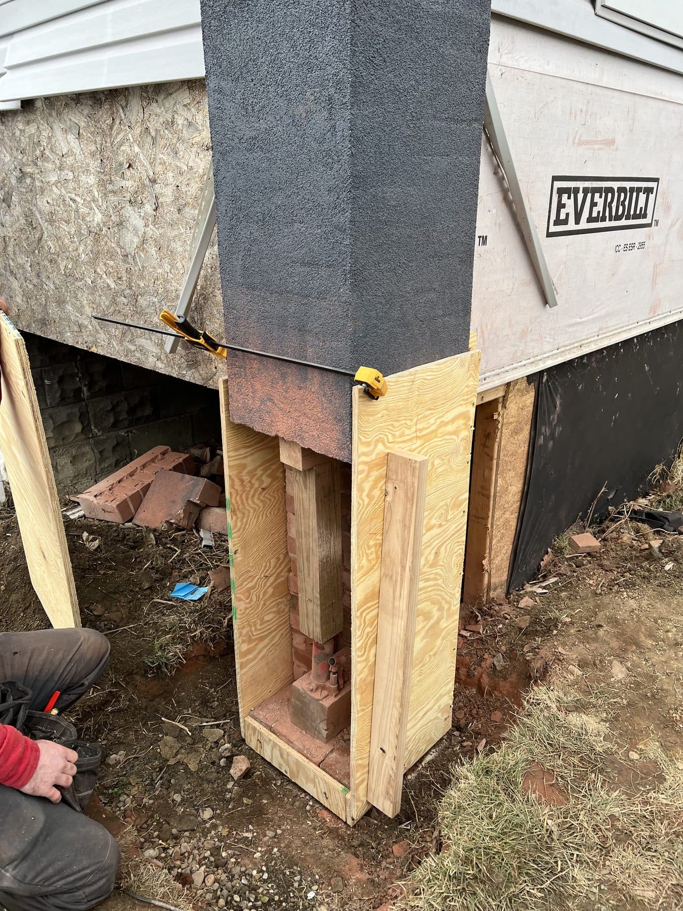 A steel jack and post carrying the brick pier inside a plywood form during a foundation rebuild