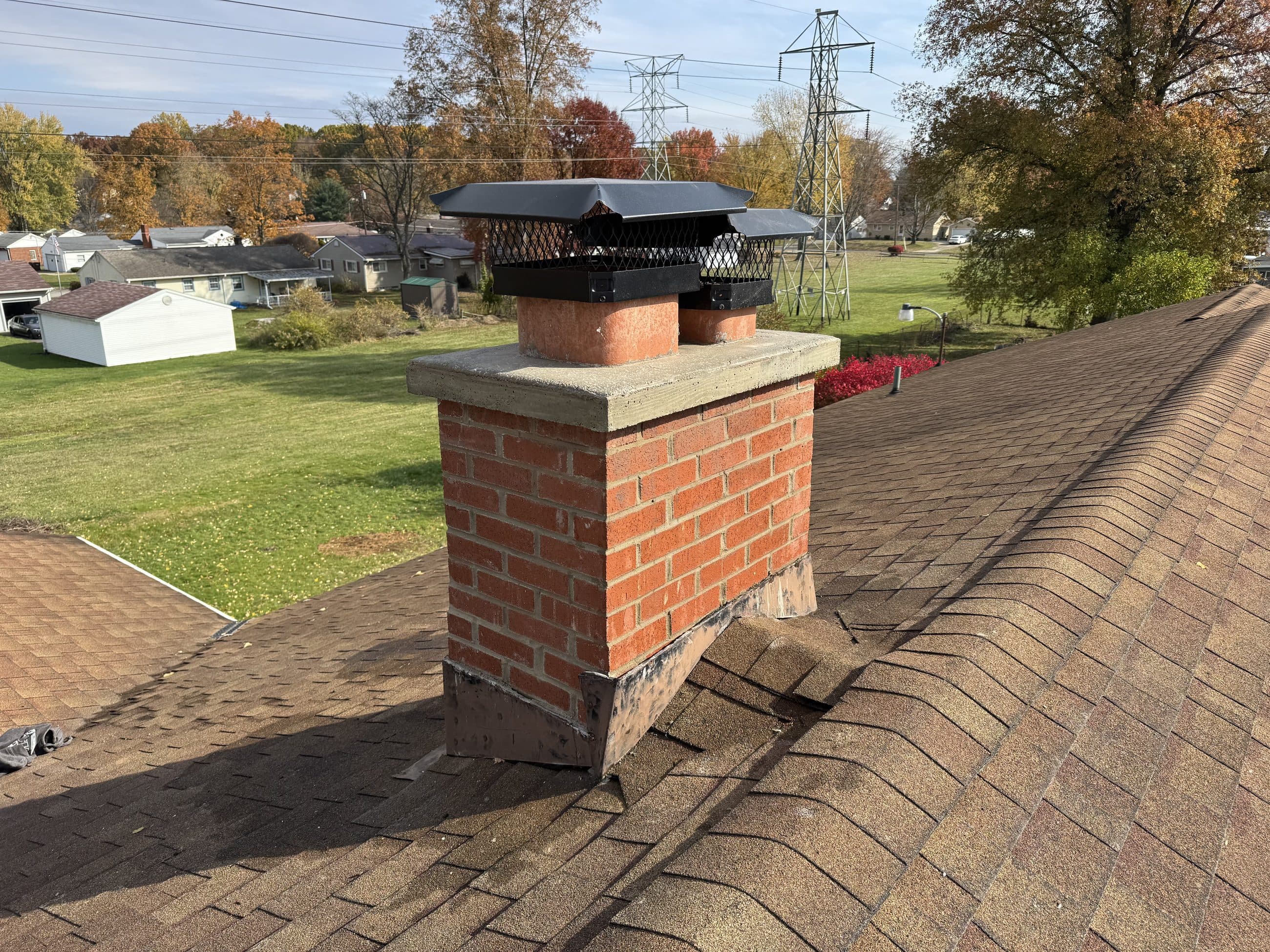 Rebuilt red brick chimney with a new concrete crown and cap, overlooking a Mahoning Valley neighborhood in autumn